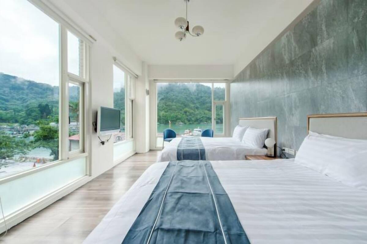 A hotel room with two beds, a TV, and a balcony with a view of the countryside.