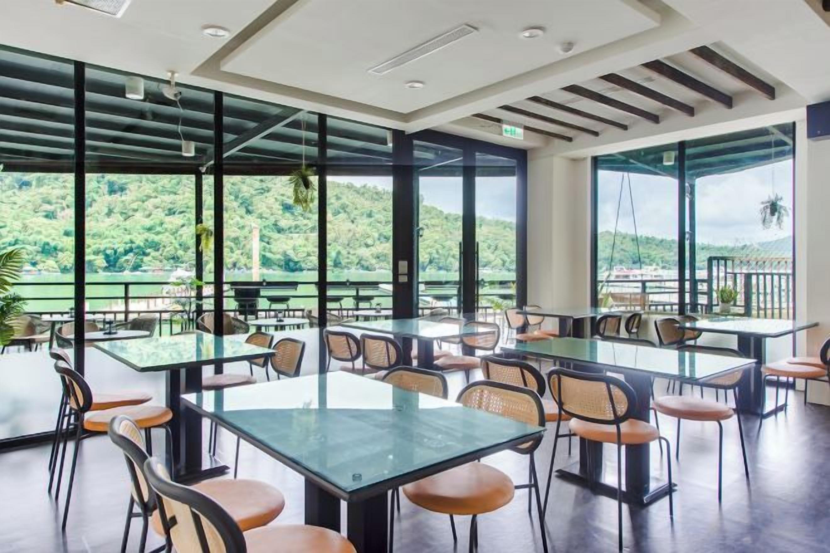 Un amplio comedor interior con mesas y sillas, ventanas grandes que ofrecen vistas a zonas verdes y un paisaje lejano.