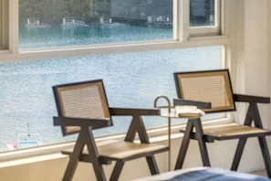 Una habitación con dos sillas orientadas a un ventanal con vista a un cuerpo de agua y barcos.