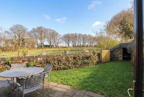 A patio with a round table and chairs, a stone wall, and a stone oven. - Kernyk (Camelford)