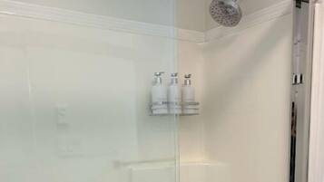 Une douche fermée par des parois en verre, avec un porte-serviettes et des articles de toilette.