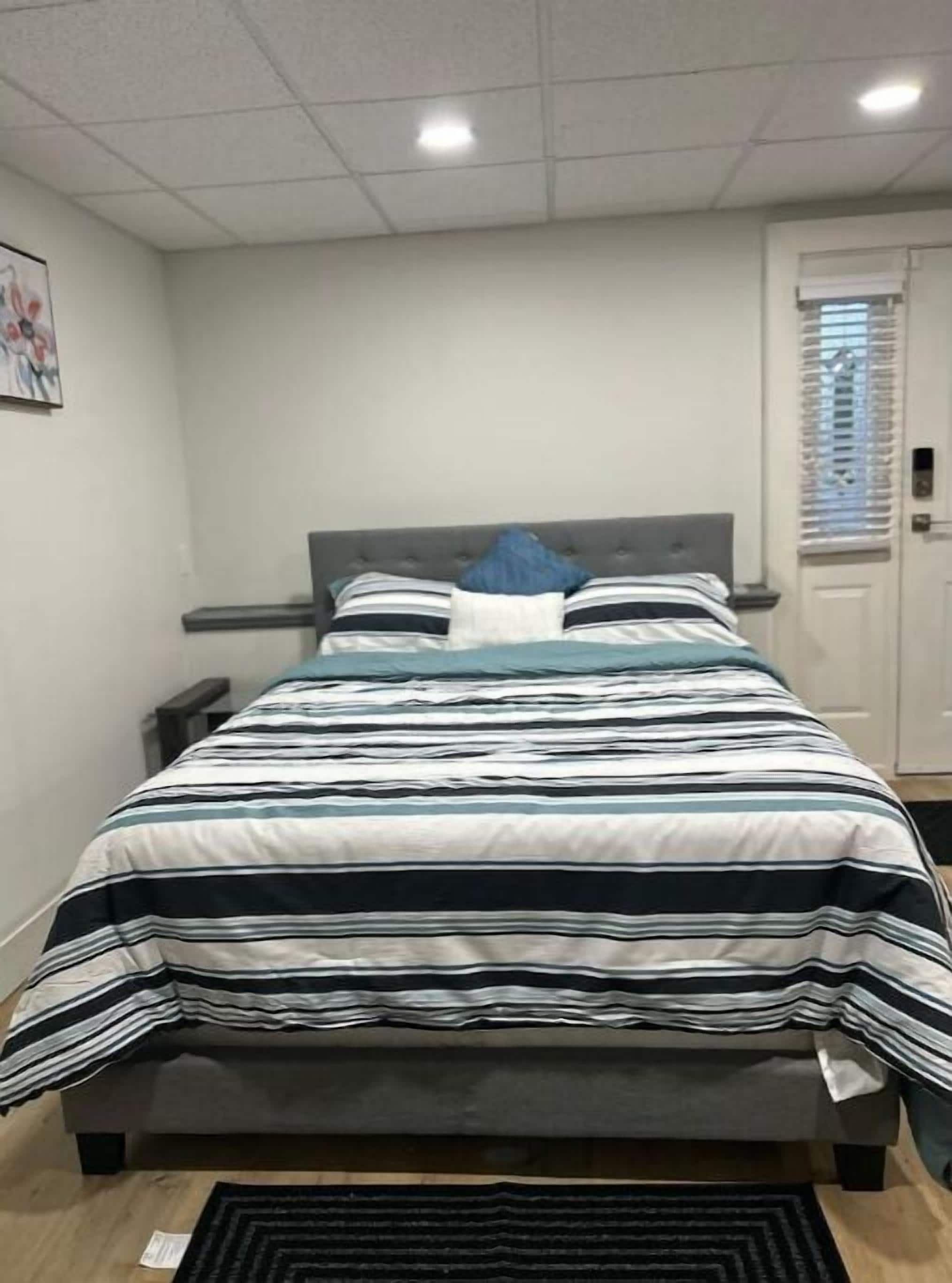 Un dormitorio con cama, mesita de noche, una puerta y una ventana con persianas.