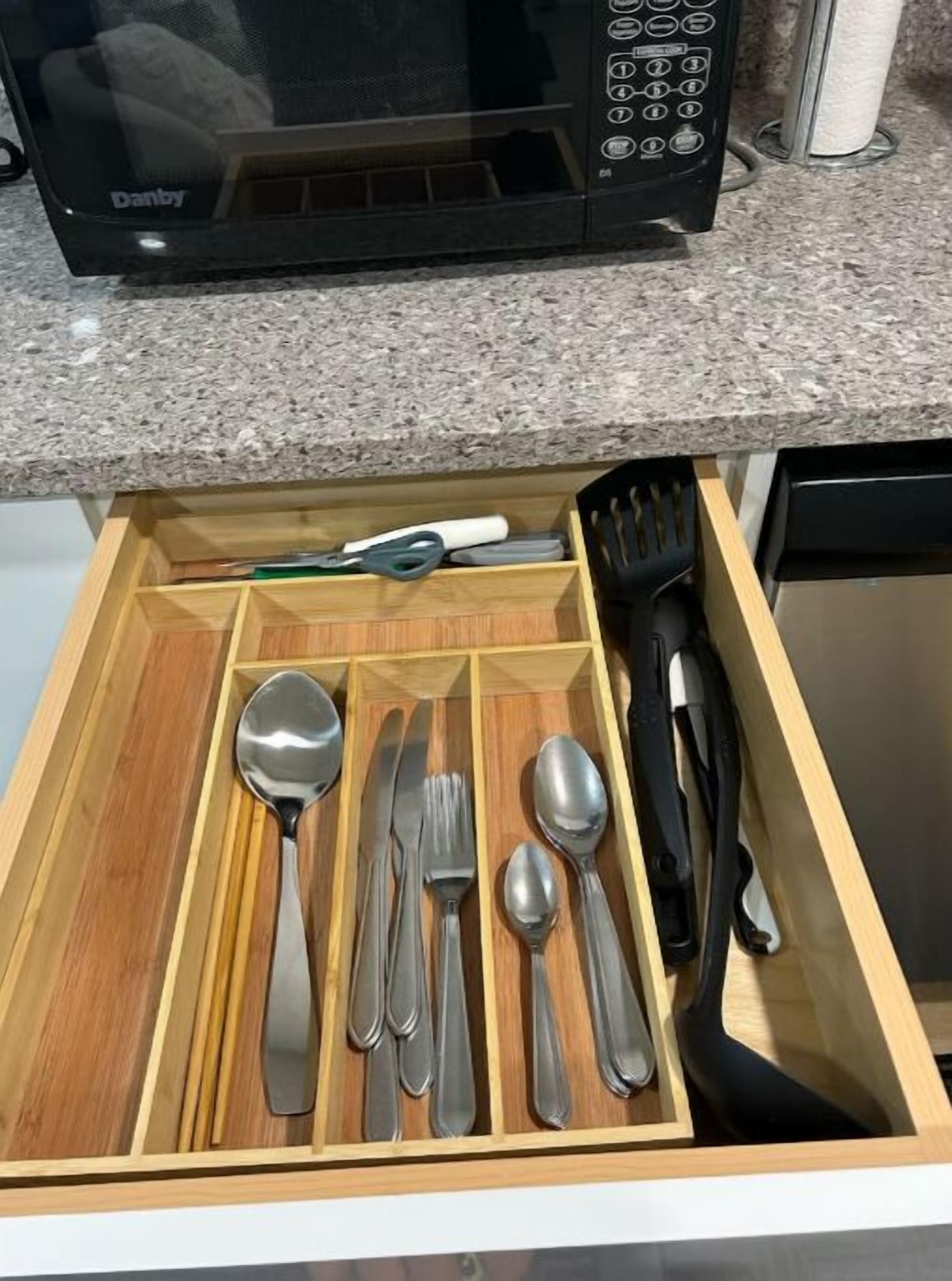 A drawer with a set of silverware neatly organized, a black spatula, and a green-handled knife.