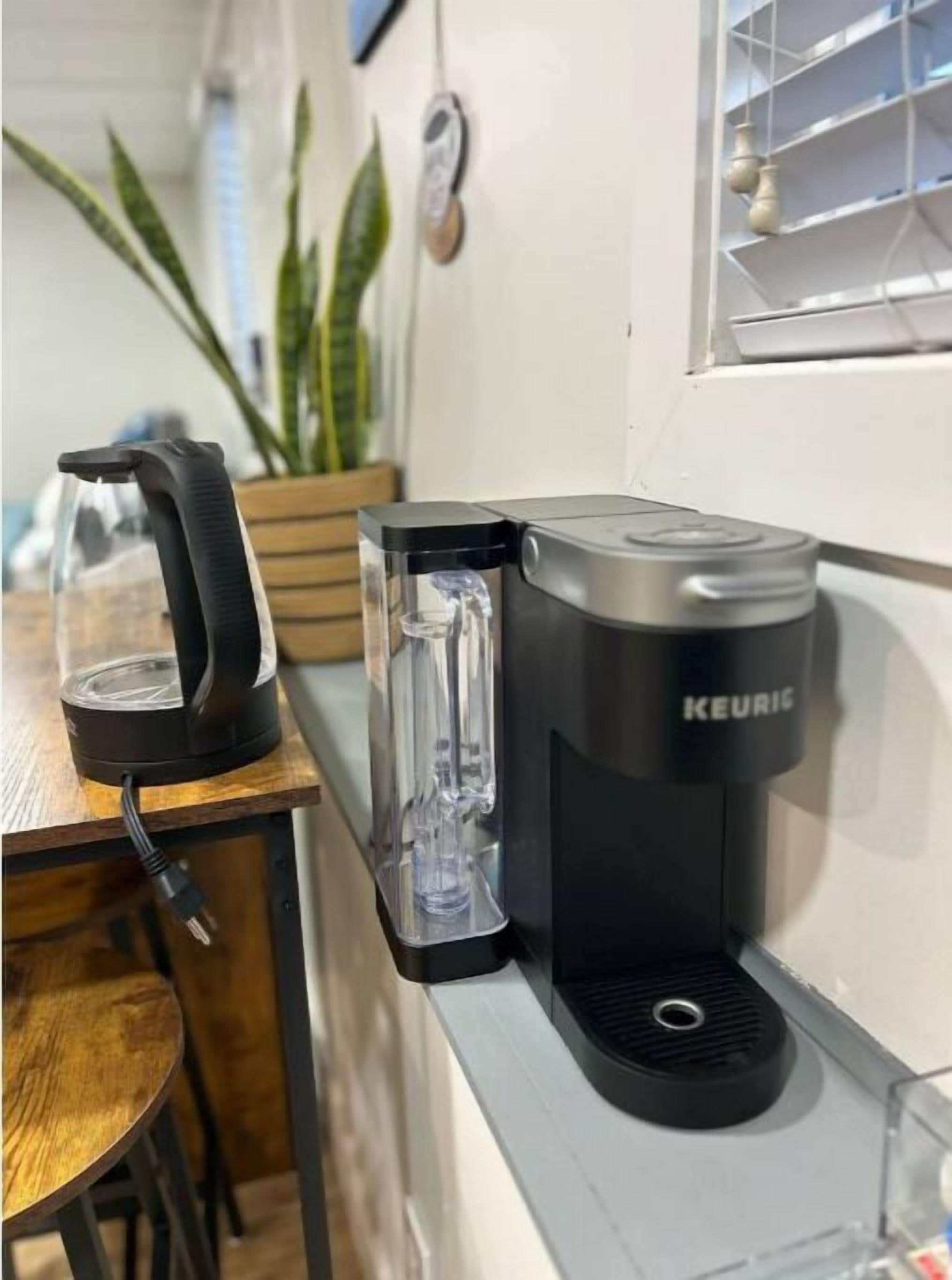 A Keurig coffee maker on a kitchen counter with a glass carafe and a black coffee pot.