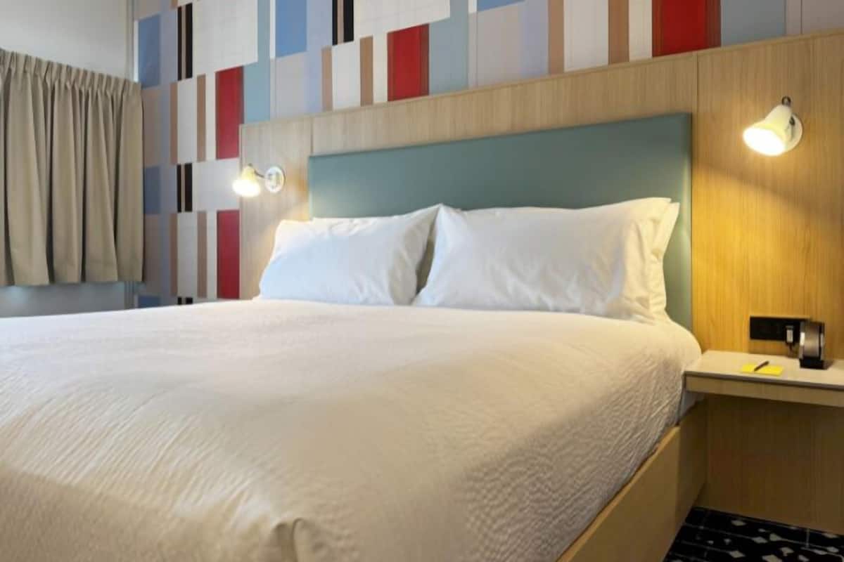 A hotel room with a bed, a nightstand, and a wall with a geometric pattern.