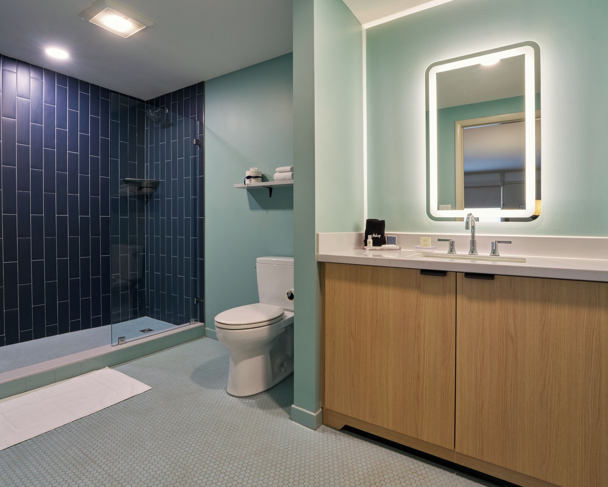 A bathroom with a shower, toilet, vanity, and a mirror.