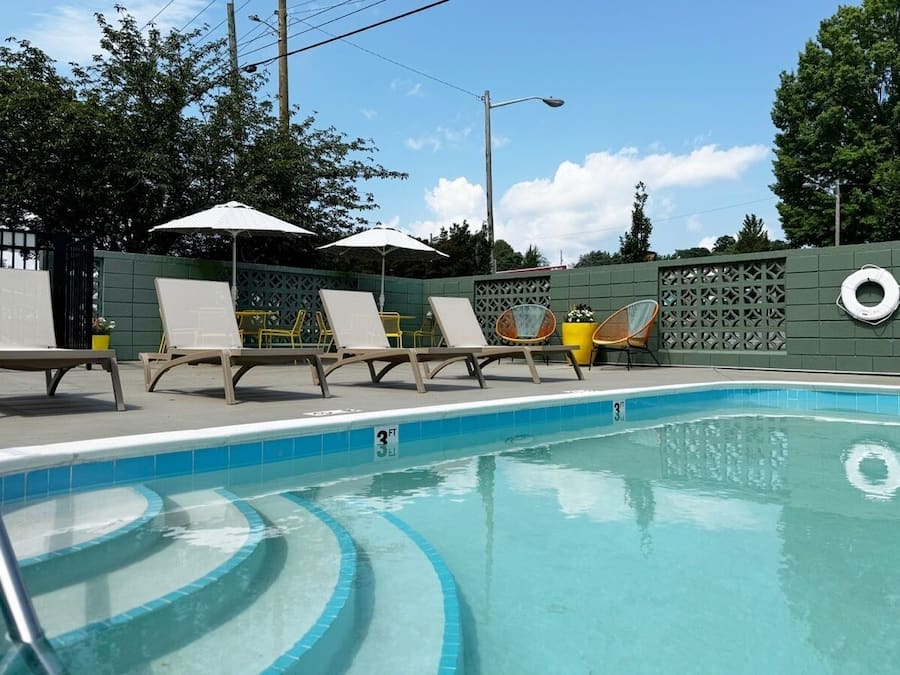 Una piscina con sillas de descanso y sombrillas, rodeada por una cerca y árboles.