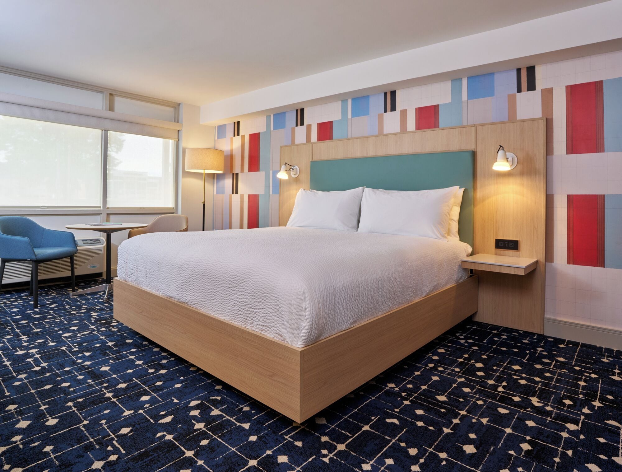 A hotel room with a large bed, a desk with a chair, and a window.