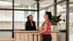 A reception desk with a wooden counter, a yellow suitcase, and a potted plant. - Colony House Motor Lodge (Roanoke)