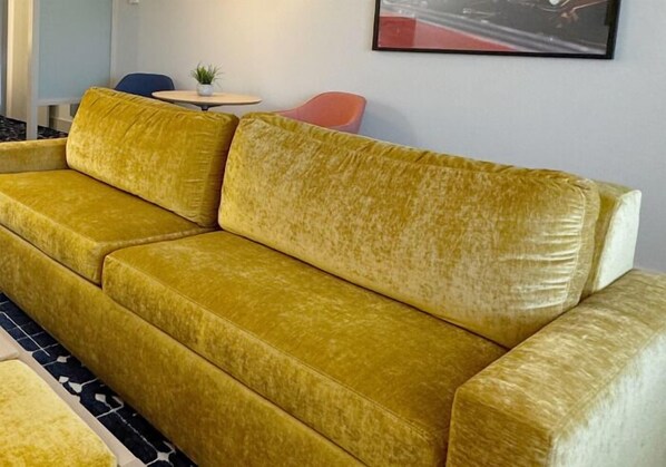 Un sofá amarillo de terciopelo en una habitación con una pequeña mesa redonda y una planta en maceta.