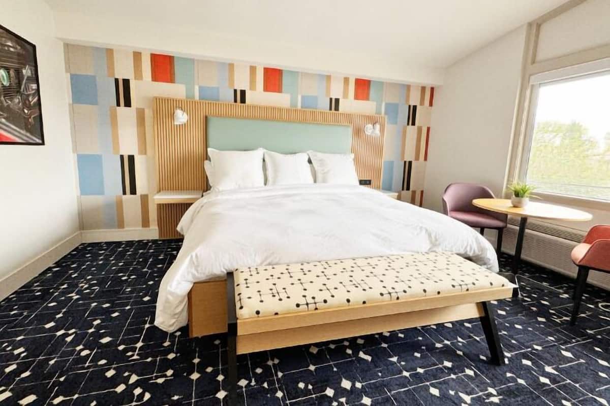 A hotel room with a bed, a bench, a small table, and a chair.
