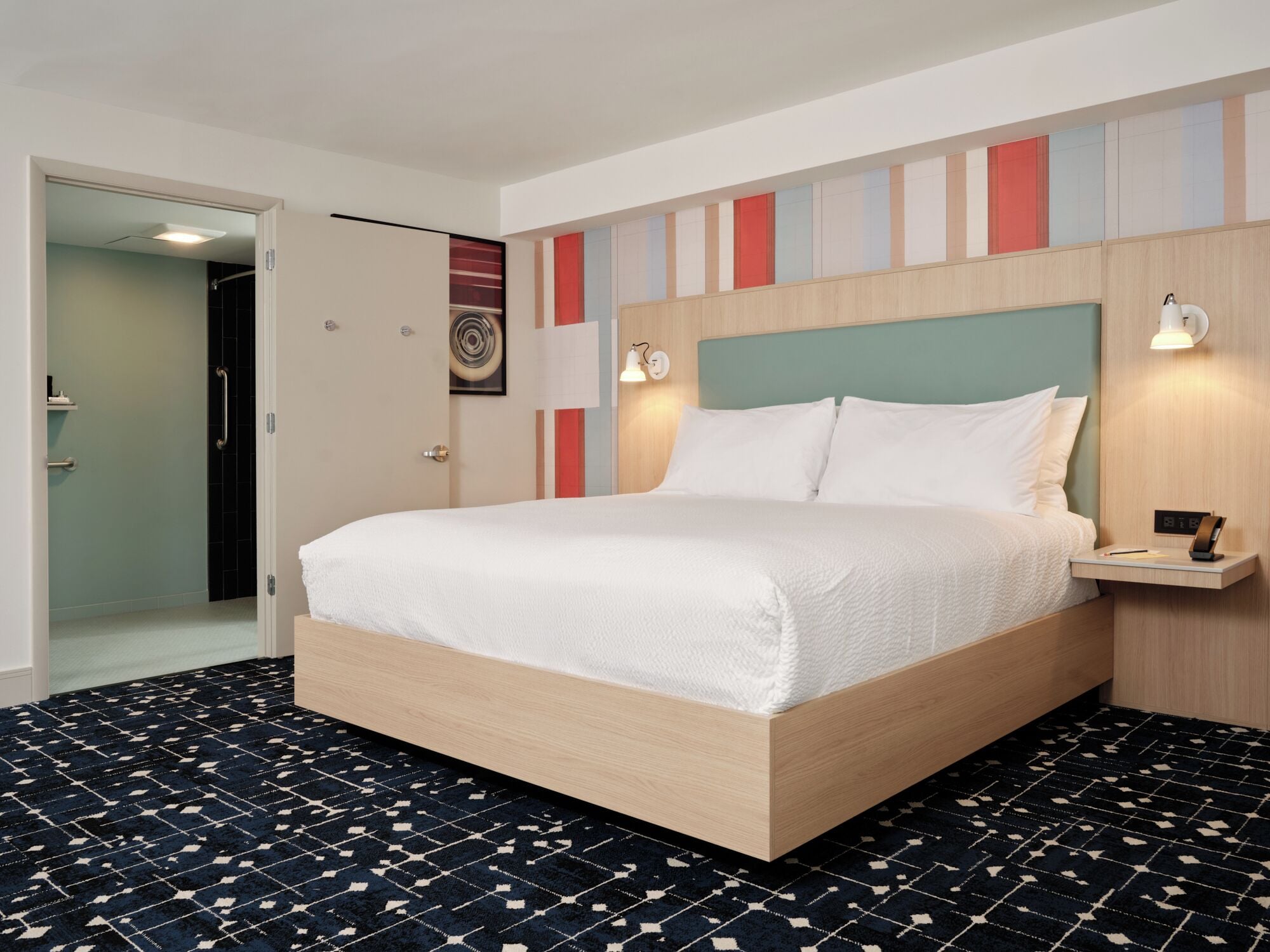 A hotel room with a bed, bedside table, wall-mounted light, and a patterned carpet.