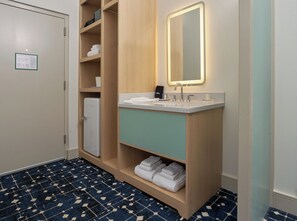 A modern bathroom with a wooden vanity, a mirror with backlighting, a white sink, and a blue patterned floor. - Colony House Motor Lodge (Roanoke)