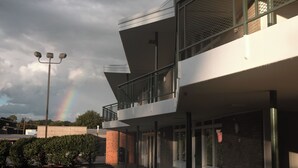A modern building with a glass balcony, a parking lot, and a rainbow in the background. - Colony House Motor Lodge (Roanoke)