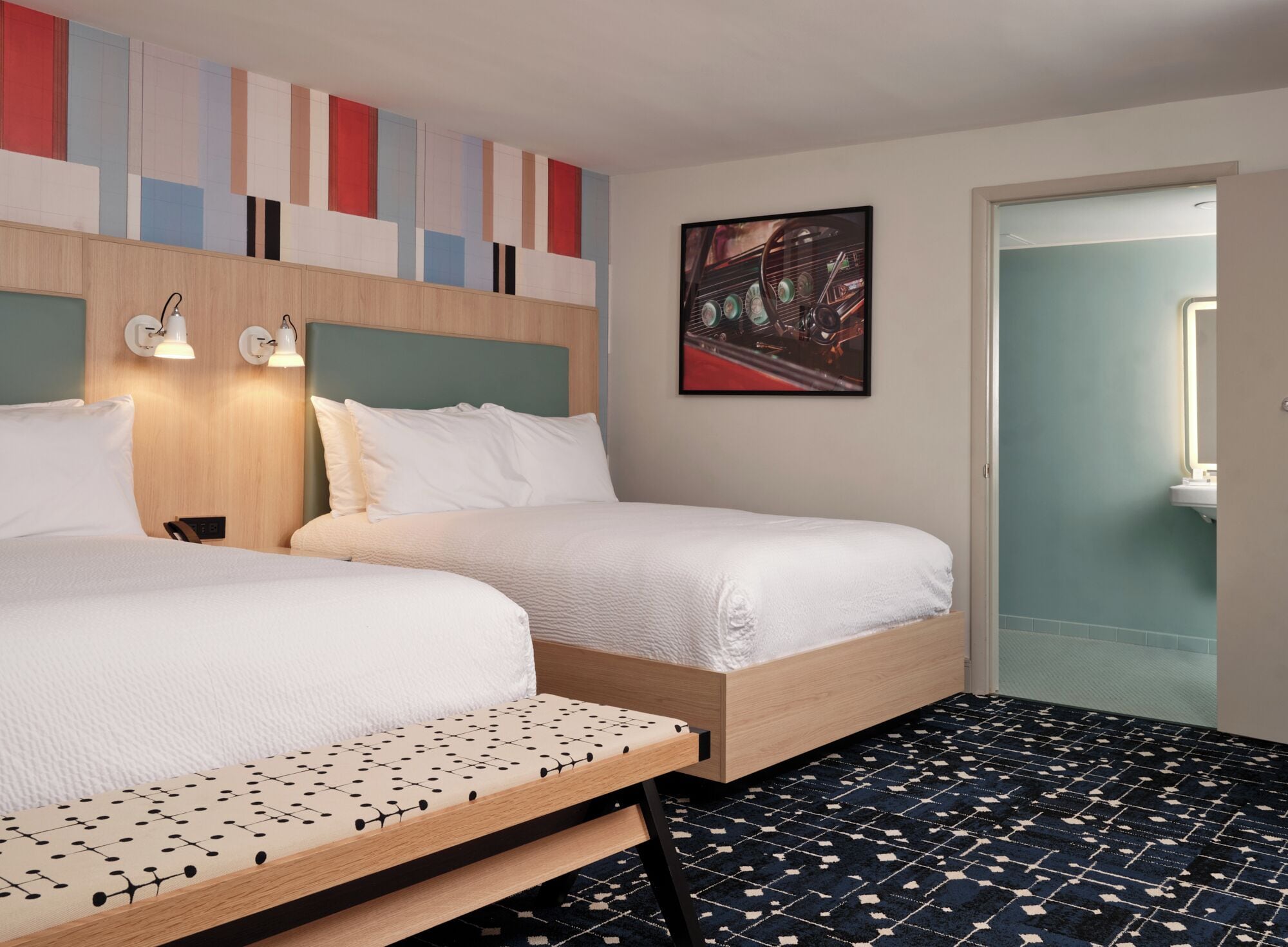 Een hotelkamer met twee bedden, een kamerkleed met een patroon en een muur met een geometrisch ontwerp.