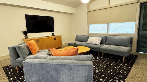 A modern living room with a grey sofa, a coffee table, and a television on a wooden cabinet. - Colony House Motor Lodge (Roanoke)