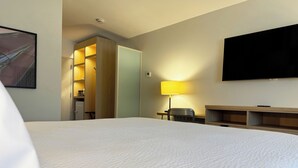 A hotel room with a large bed, a desk, a chair, a TV mounted on the wall, and a door leading to a kitchenette. - Colony House Motor Lodge (Roanoke)