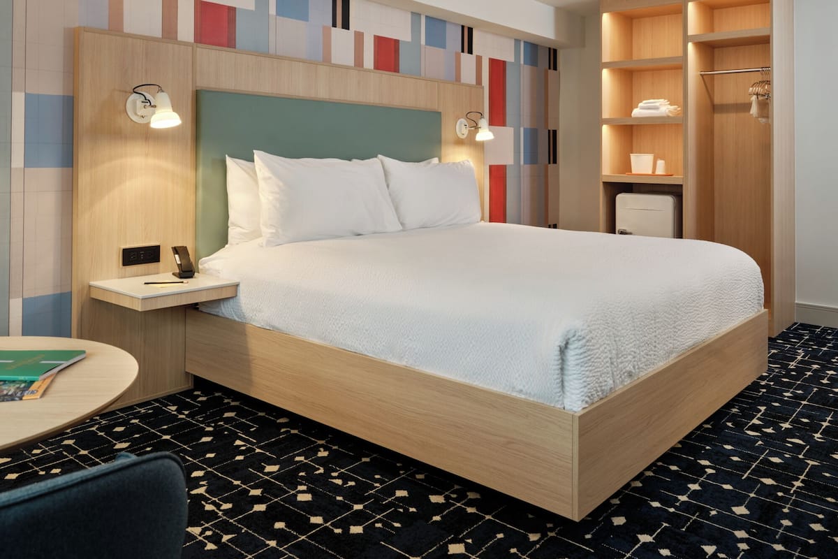 A hotel room with a bed, bedside tables, a desk, a chair, a wardrobe, and a patterned carpet.