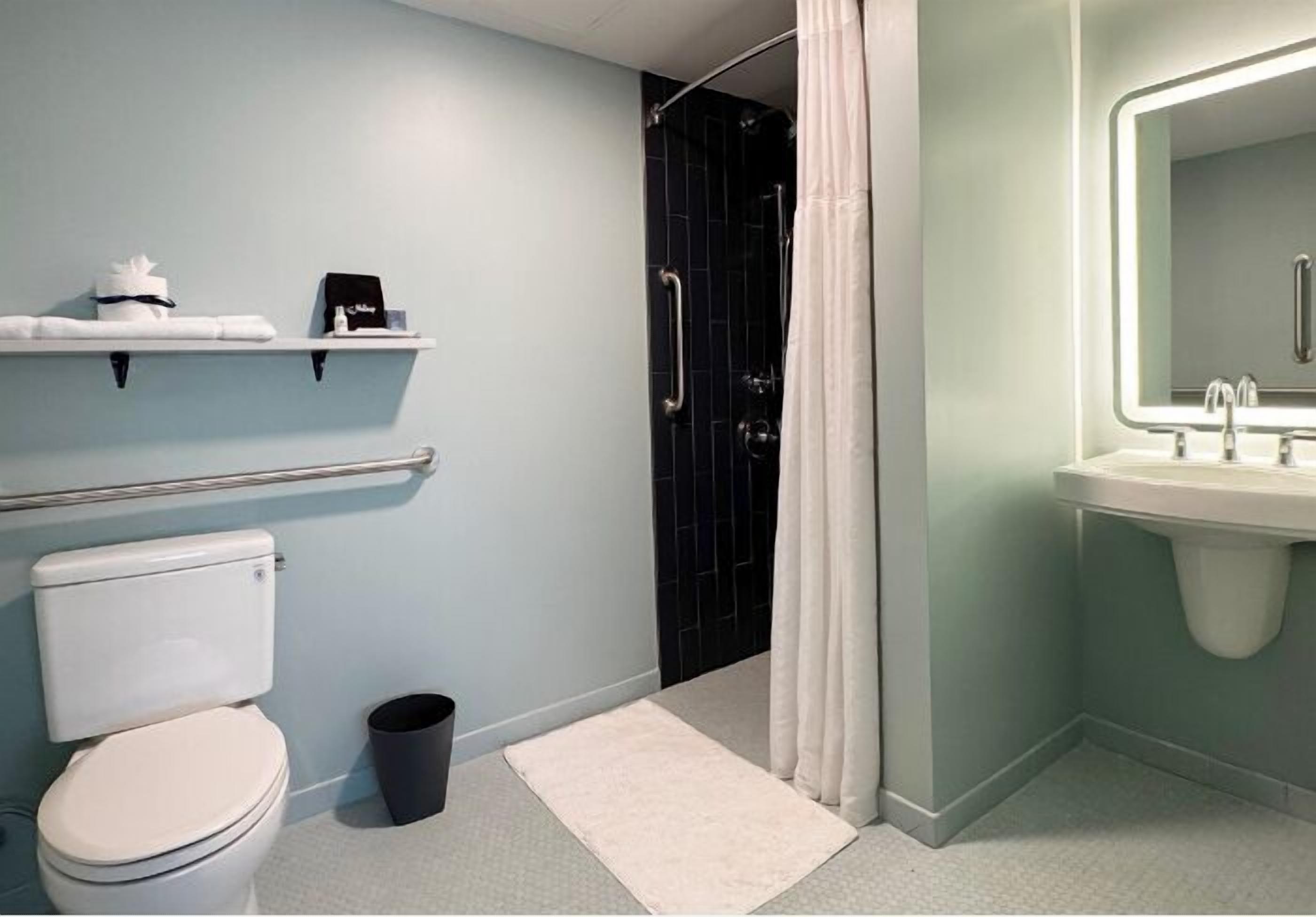 A bathroom with a toilet, a sink, a shower with a curtain, and a mirror with a light.