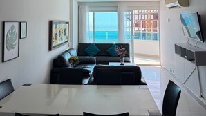 A modern living room with a sofa, dining table, and chairs. There is a large window with a view of the sea. - APARTAMENTO 702A (Cartagena)