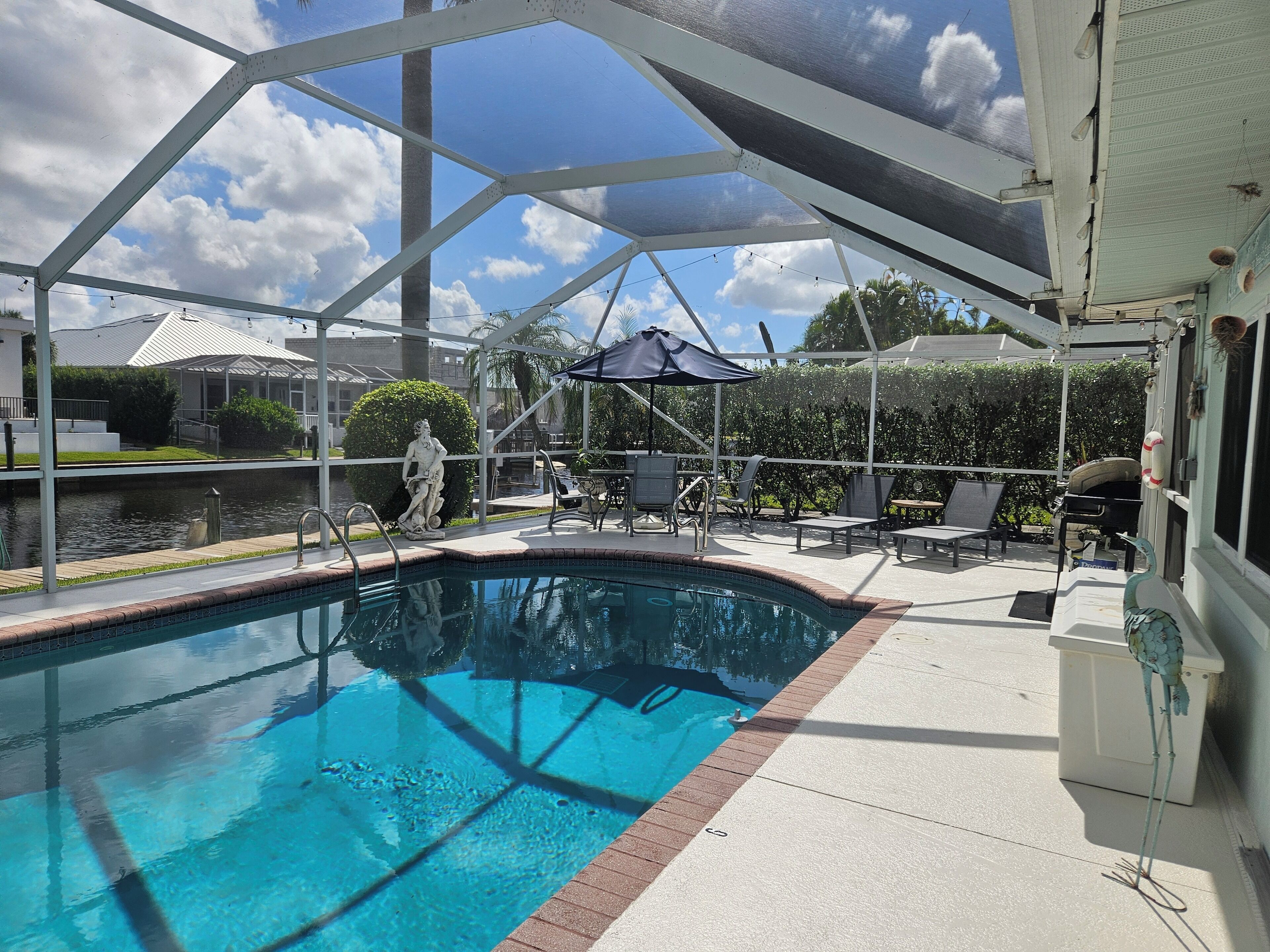 A pool area with a clear blue pool, lounge chairs, and a statue.