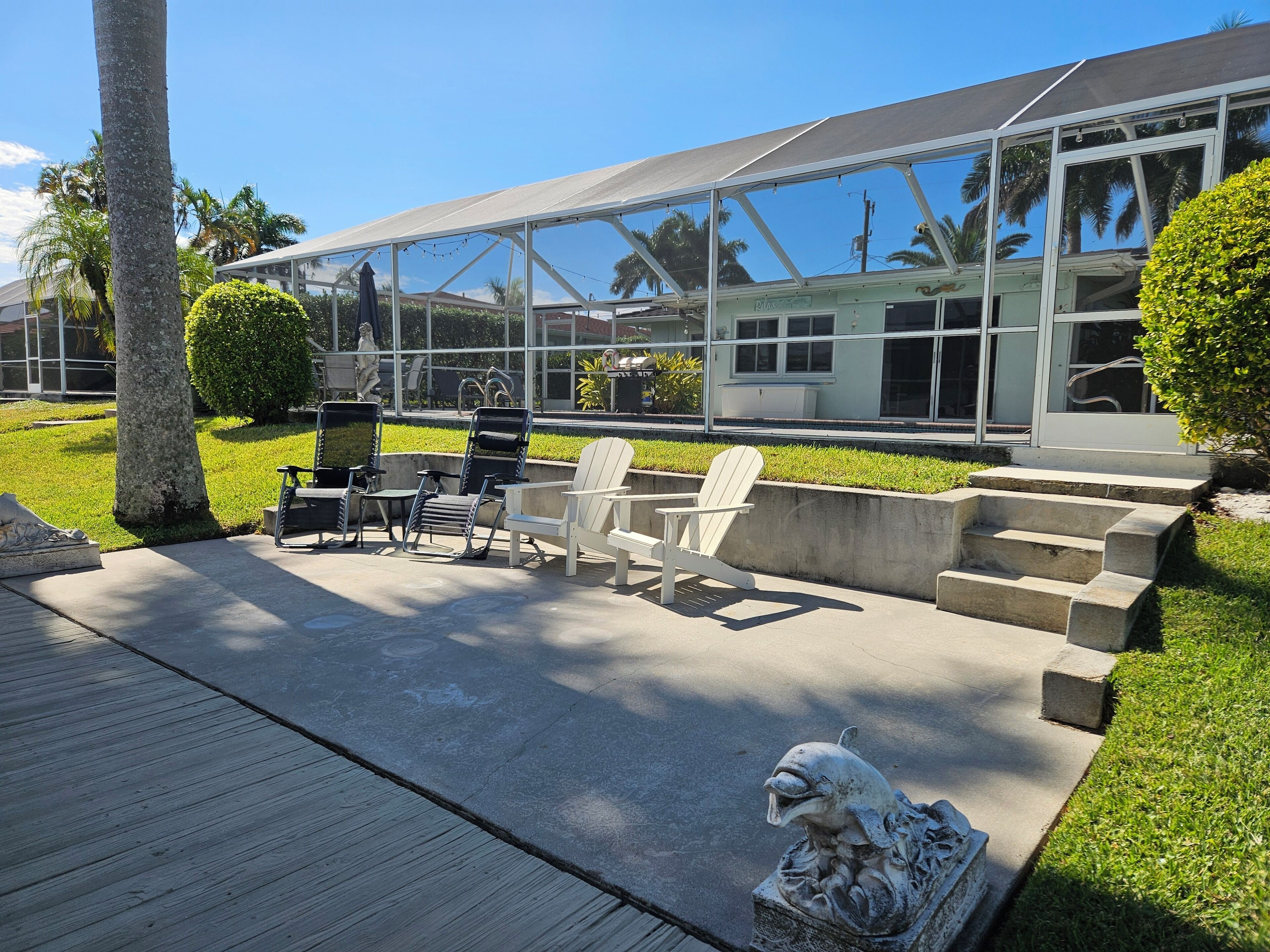 A modern outdoor patio with a glass enclosure, outdoor seating, and a decorative dolphin sculpture.