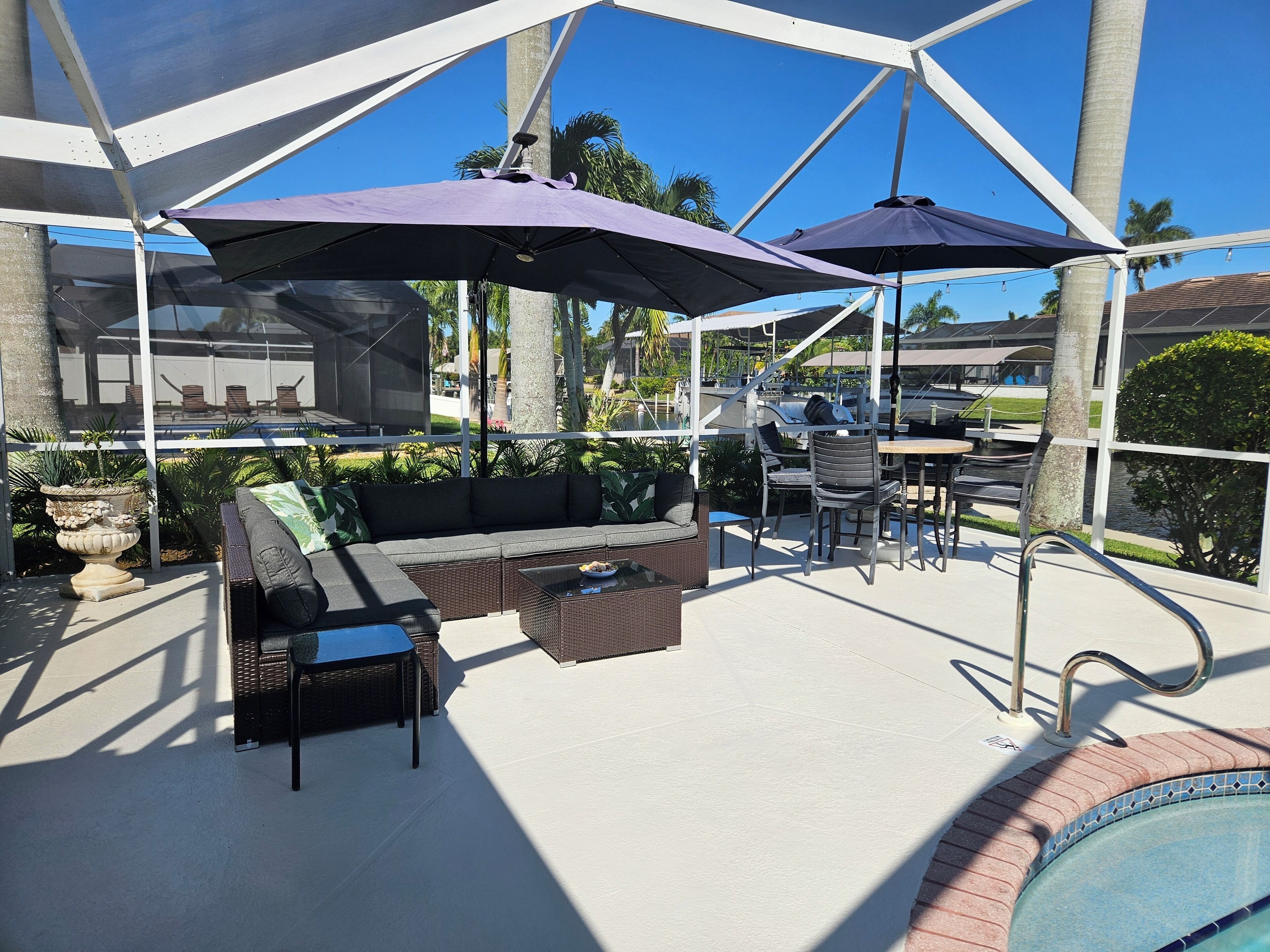 Een terras buiten met een zwembad, een overdekte zithoek en parasols.
