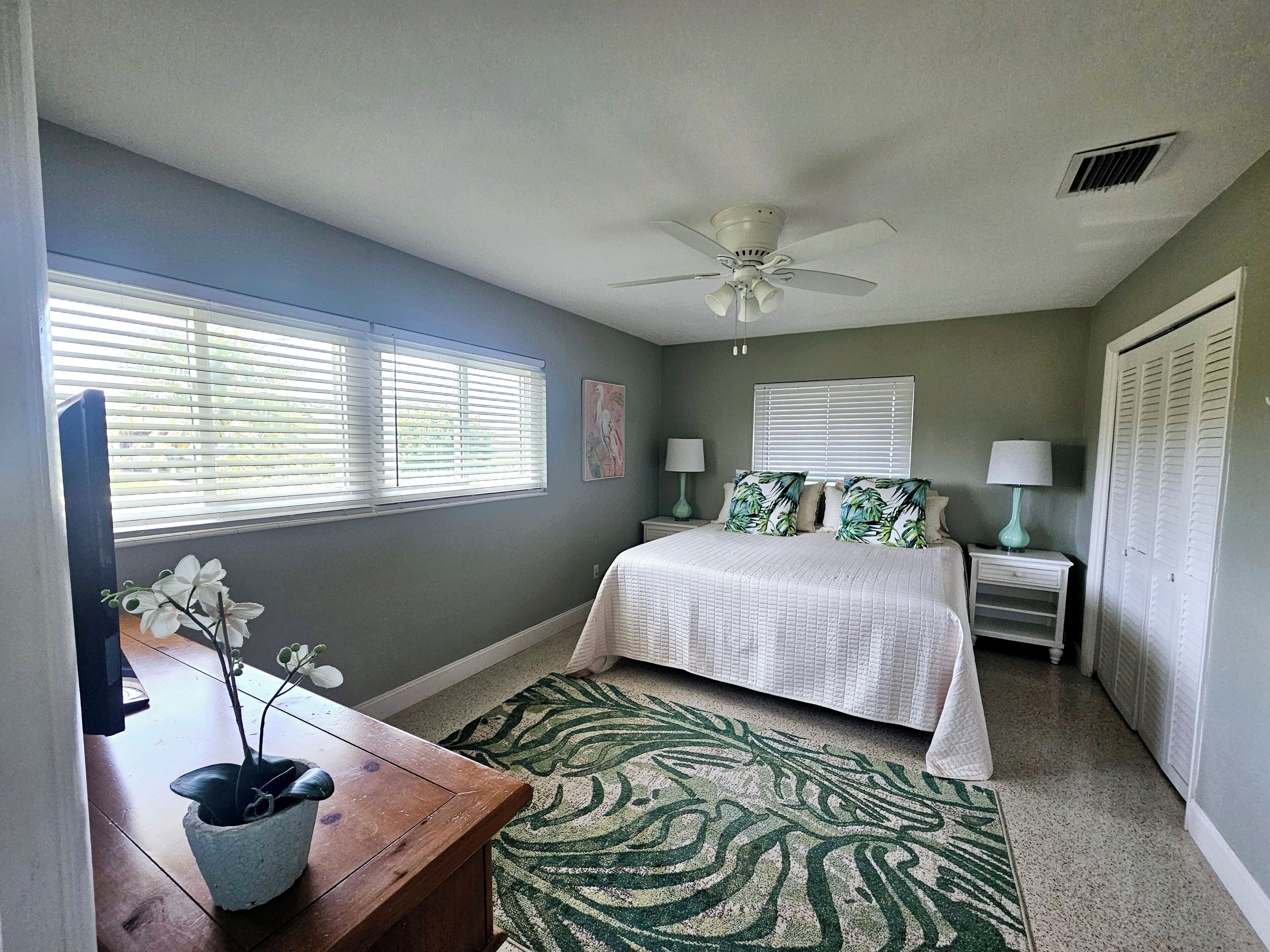 A bedroom with a bed, two bedside tables with lamps, a ceiling fan, and a window with blinds.