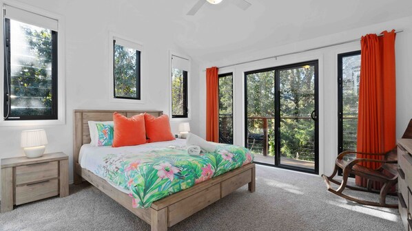 Une chambre à coucher comprenant un lit, une table de chevet, une chaise et une vue sur l’extérieur grâce à de grandes fenêtres.