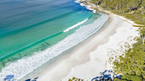Una playa con aguas turquesas cristalinas y arena blanca, rodeada de vegetación.