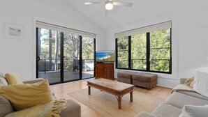 Un salón amplio con ventanas grandes, un televisor de pantalla plana y una mesa de centro de madera.
