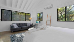 Un dormitorio moderno con una cama grande, un sofá gris, un televisor y una escalera contra la pared.