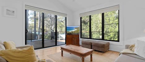 A spacious living room with large windows, a flat-screen TV, and a wooden coffee table.