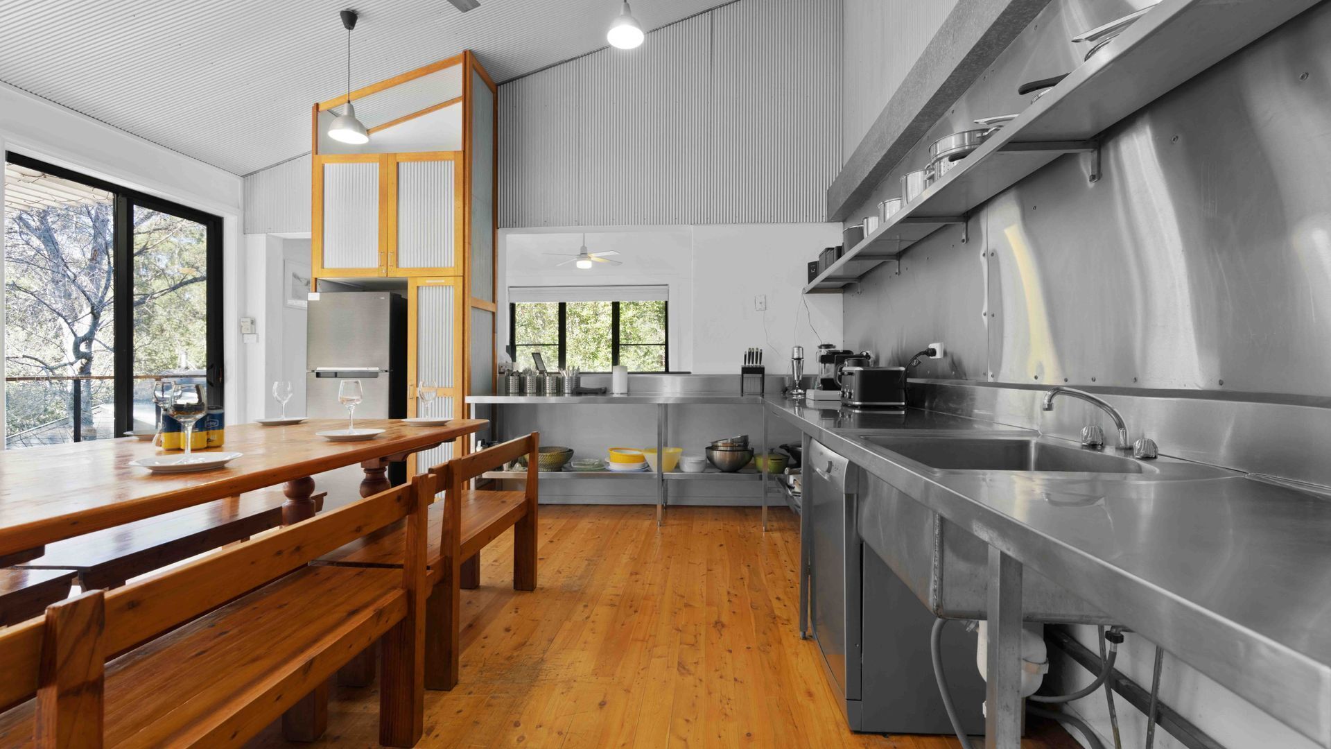 A modern kitchen with stainless steel appliances, wooden dining table, and large windows.