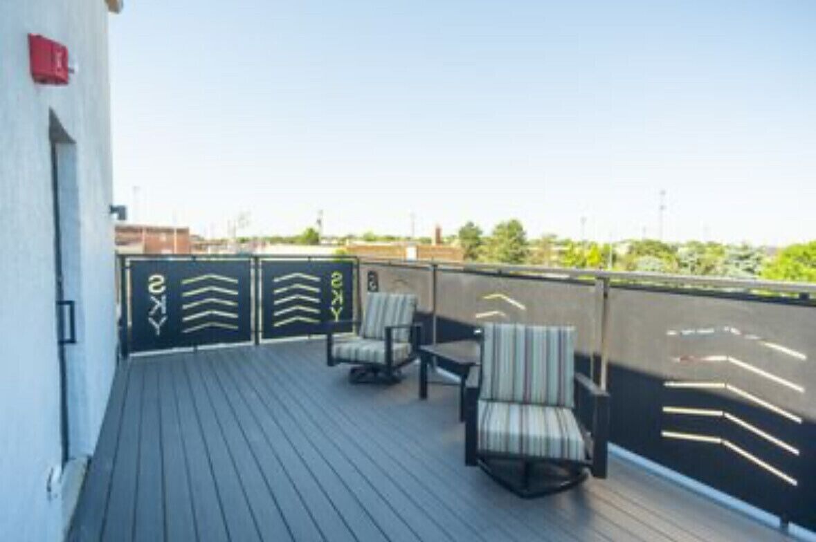 En tagterrasse med udsigt over byens skyline, med et siddeområde med stole og et bord.