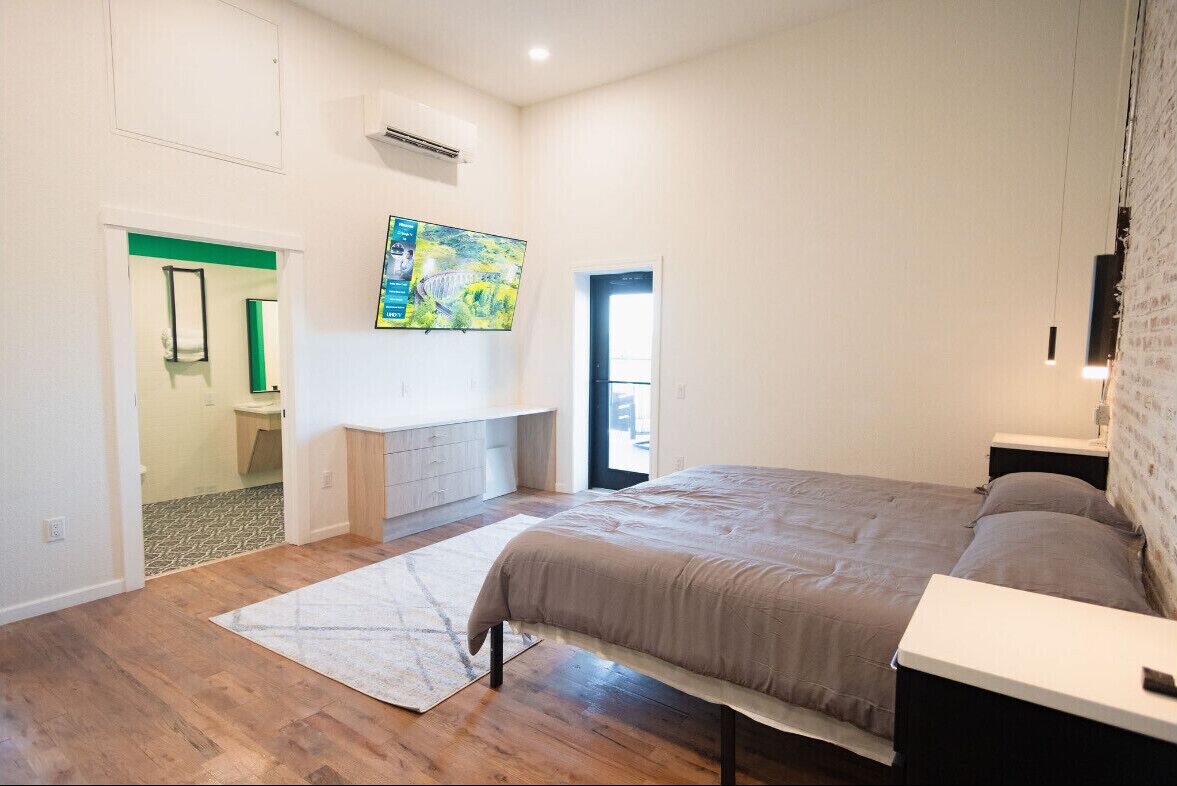 A bedroom with a large bed, a desk, and a painting on the wall.