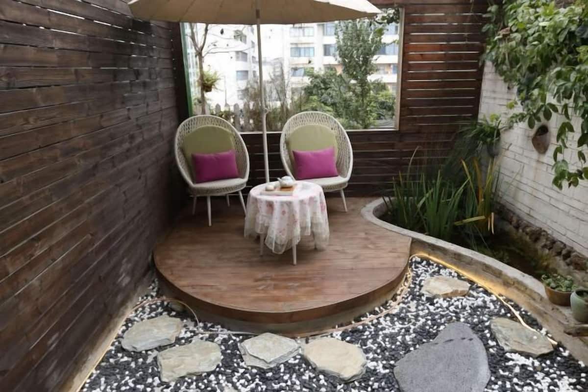 A small patio area with two wicker chairs, a round table, and a small garden with pebbles and plants.