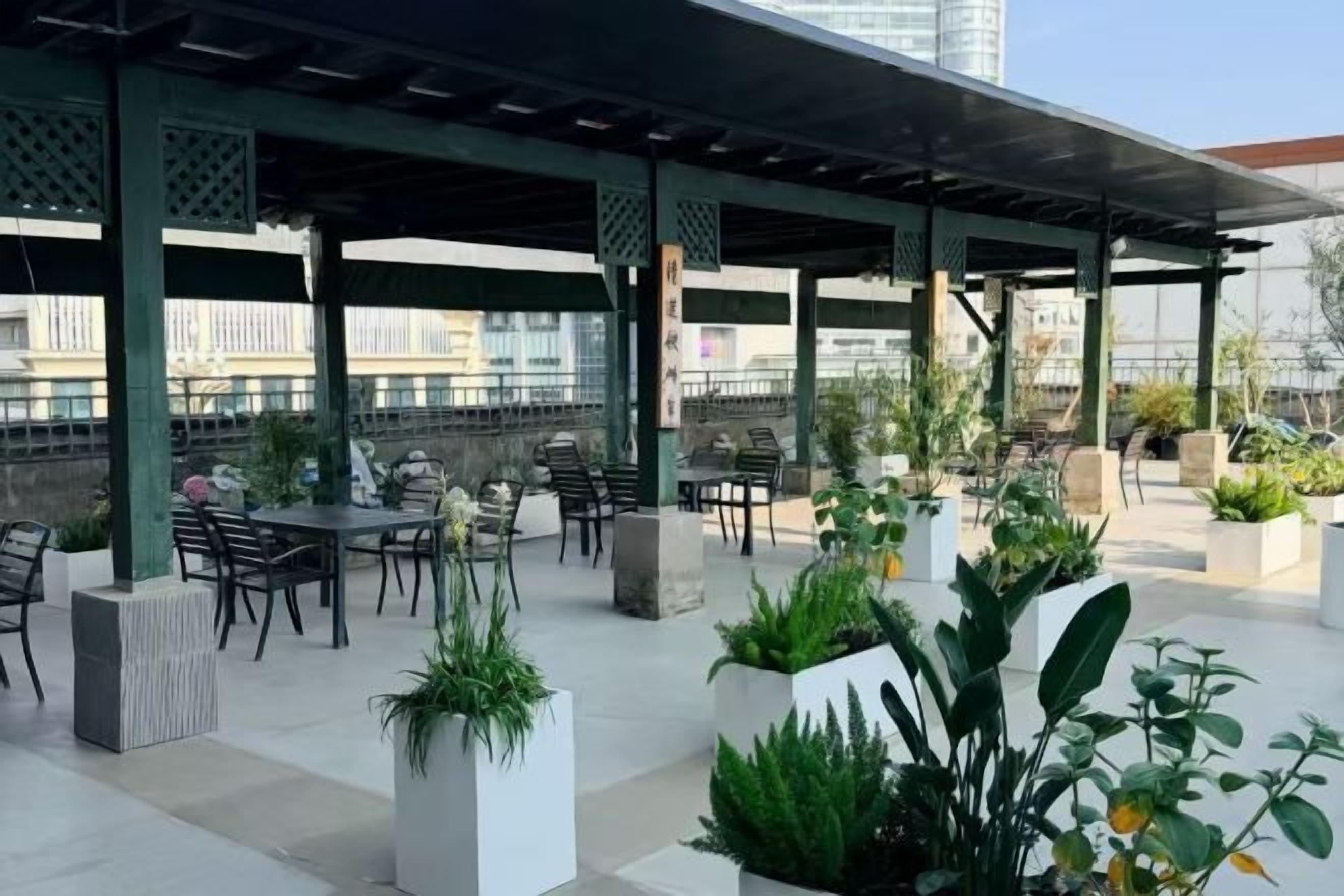 An outdoor seating area with tables and chairs, surrounded by potted plants.