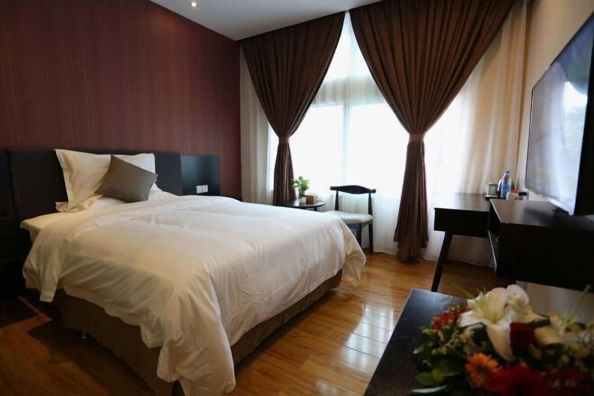 A hotel room with a large bed, a desk, a chair, and a small table with a flower arrangement.