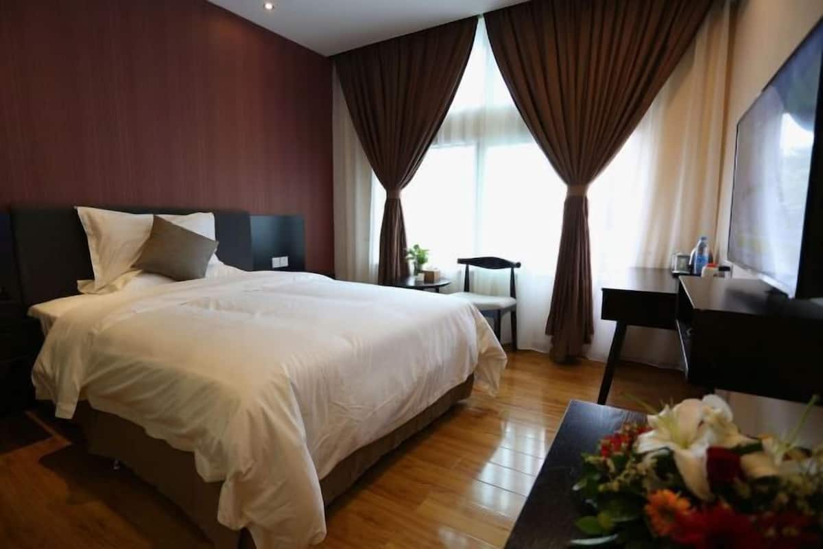 A hotel room with a large bed, a desk, a chair, and a small table with a flower arrangement.