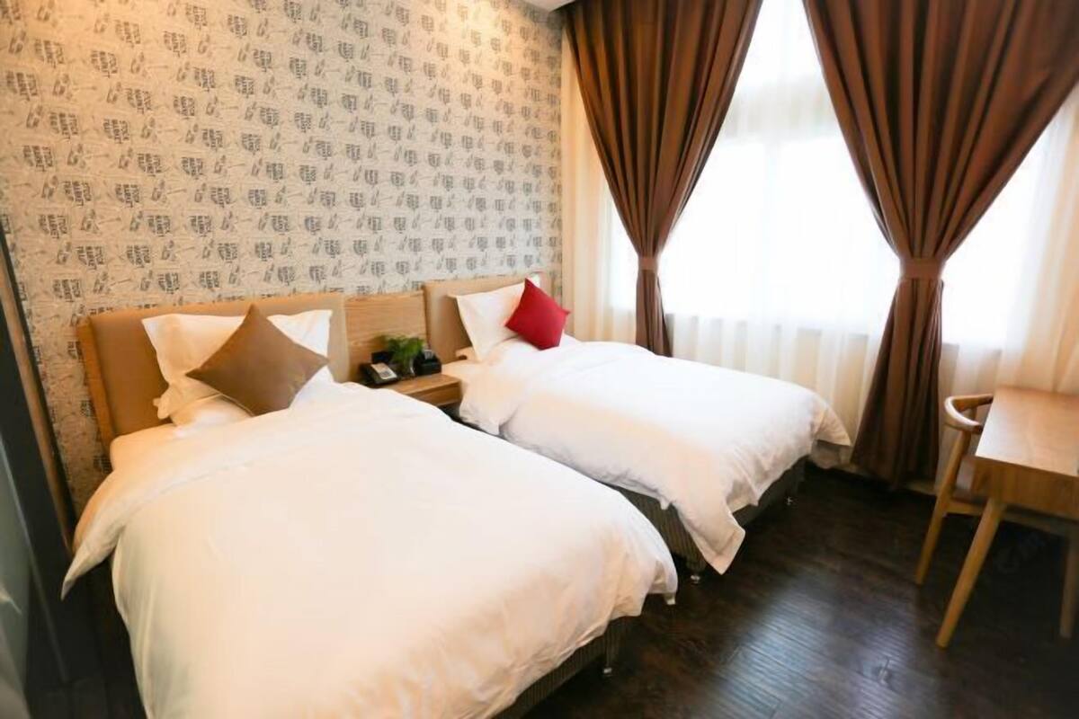 A hotel room with two beds, a wooden nightstand, a chair, and a patterned wallpaper.