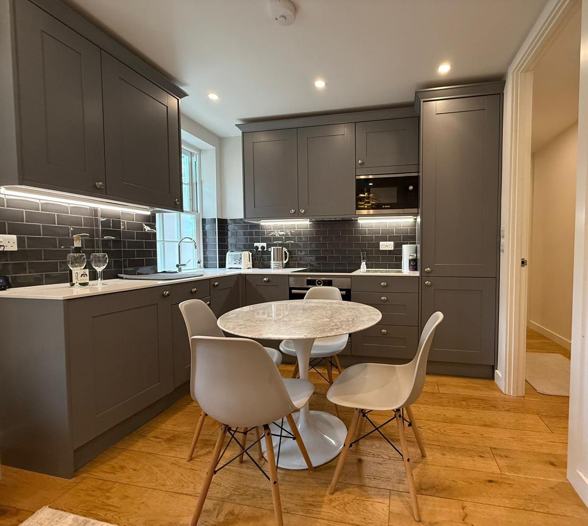 A modern kitchen with dark cabinetry, a round marble table, and four chairs.