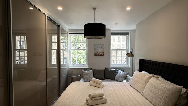 A bedroom with a large bed, a black headboard, and a window with a view of trees. - Central London Apartment With 2 Bedrooms -sleeps 6 (London)