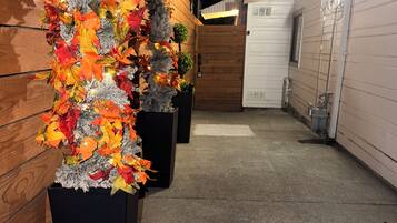 Une rangée de jardinières noires ornées de feuilles d’automne et d’un petit arbre, disposées contre un mur en bois.