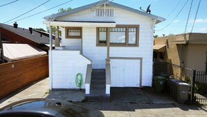 Uma casa pequena, térrea, com varanda frontal, porta de garagem e antena parabólica.
