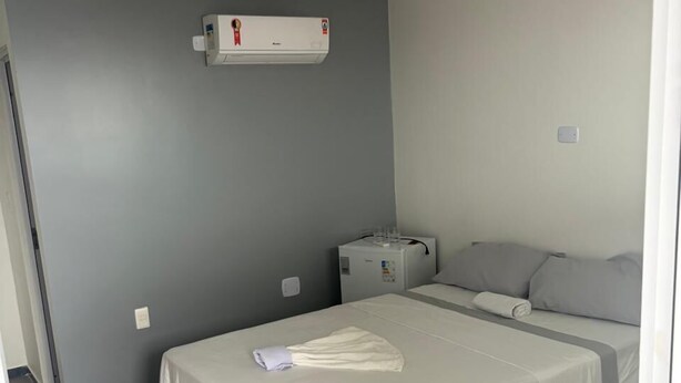 A small, clean room with a bed, a heater, and a small table. - Hospedagem Praia do Forte (Tamandaré)
