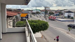 A balcony overlooking a street with buildings and a parked yellow truck. - Hospedagem Praia do Forte (Tamandaré)