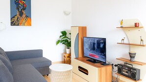 Ett modernt vardagsrum med en grå soffa, en tv-apparat på ett träställ, en växt och en bokhylla med dekorativa föremål.