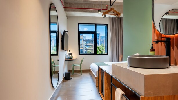 Habitación de hotel moderna con un ventanal grande, un lavamanos redondo, un espejo y una silla.