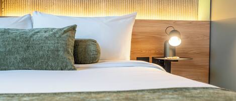Una cama bien hecha con almohadas, una mesita de noche con lámpara y un cabecero de madera.